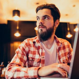 Youn g bearded man working on laptop in a bar